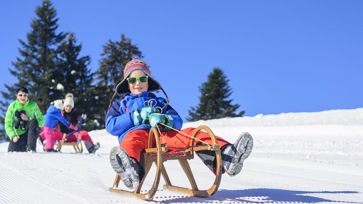 Pista da slittino a San Candido, in primo piano - un bambino siede con occhiali da sole sulla sua slitta